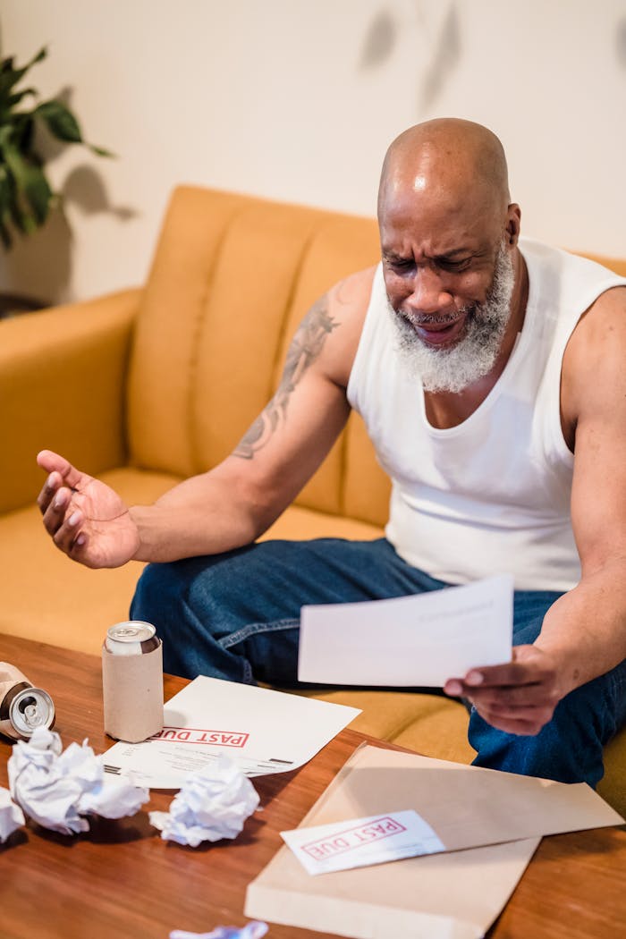 An African American man showing distress over unpaid bills, highlighting financial struggles.